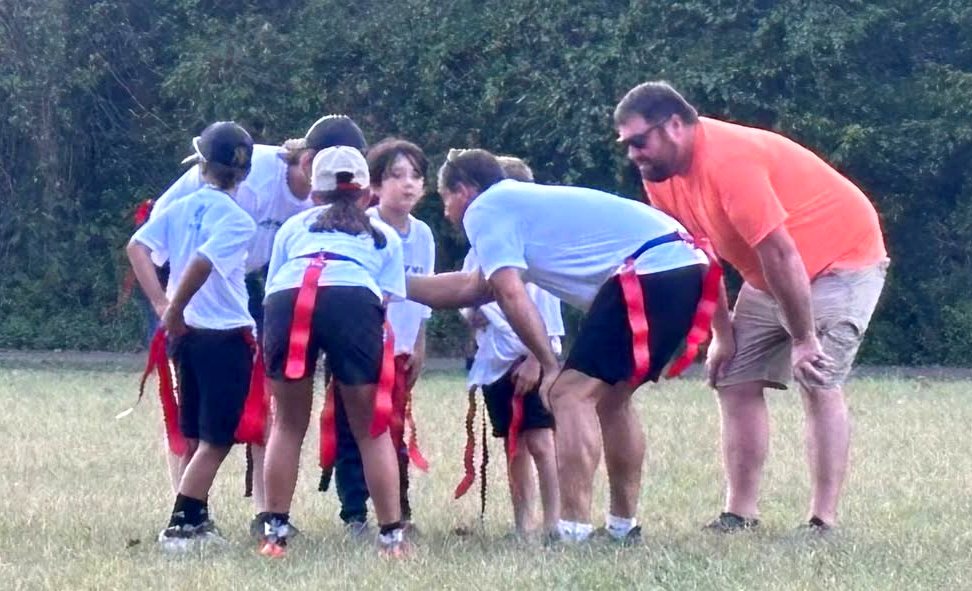 Kids and coaches in a flag football huddle
